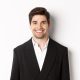 Close-up of handsome young businessman in trendy suit smiling, standing against white background.
